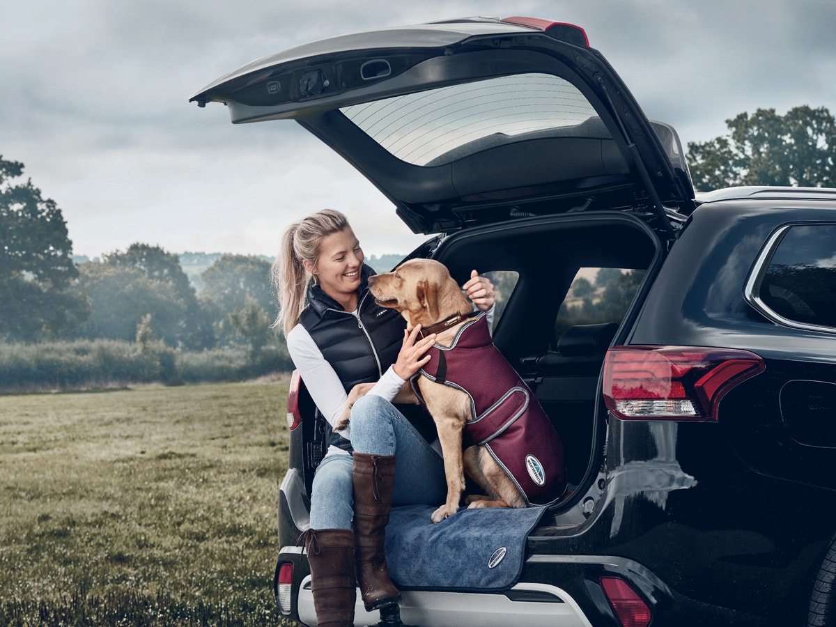 Woman sitting with dog wearing WeatherBeeta dog coat in boot of car
